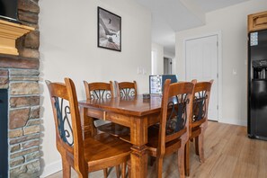 A dining area with a wooden table and chairs, a stone wall, a black refrigerator, and a door in the background. - Lakeside Escape LS 36B 2 BR |Pineview Res |Hot Tub (Huntsville)