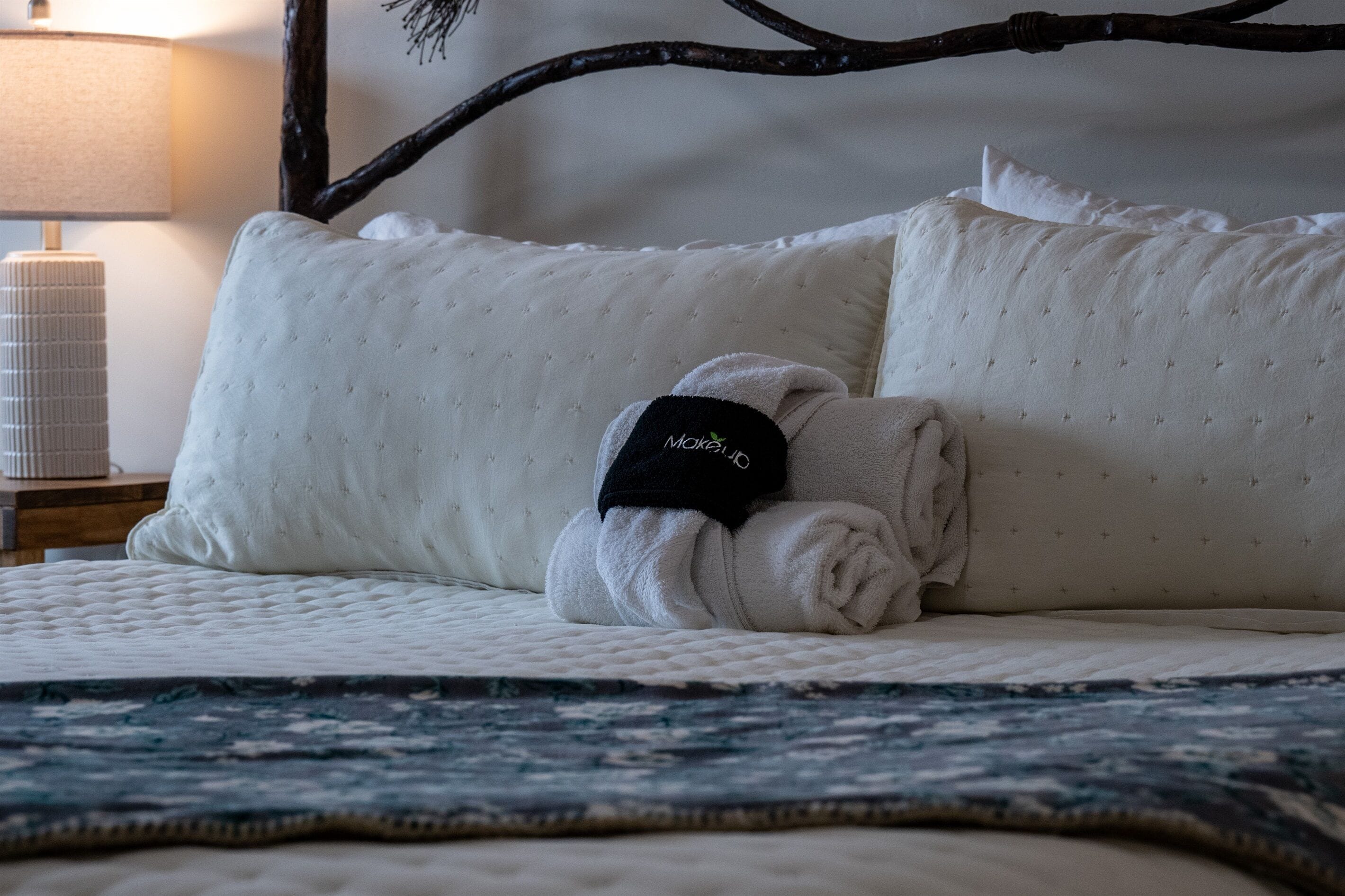 A bed with a quilted white mattress, a folded white towel, and a black tag with 'MOKO' on it.