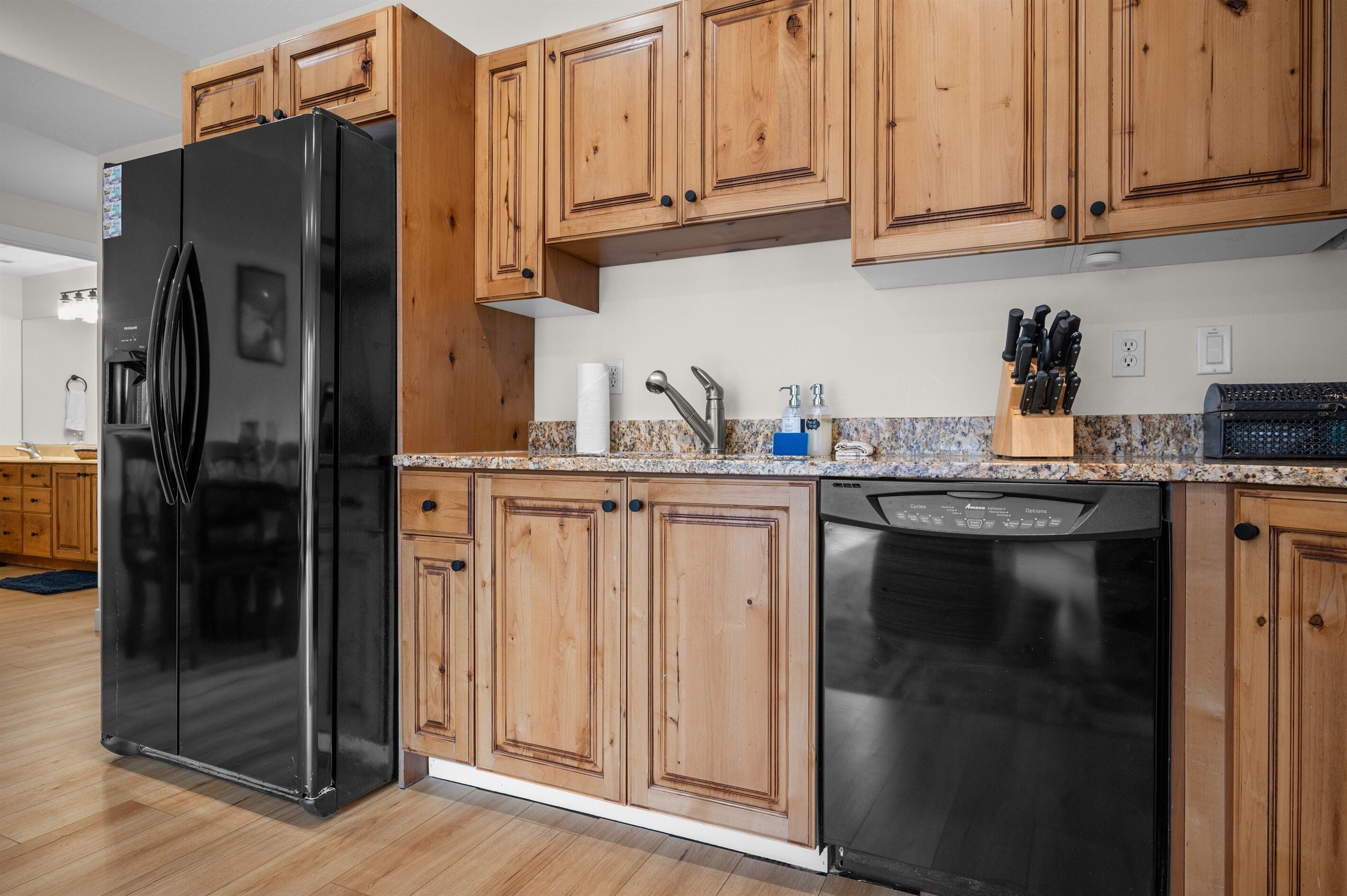 A kitchen with wooden cabinets, a black refrigerator, a dishwasher, and a granite countertop.