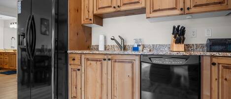 A kitchen with wooden cabinets, a black refrigerator, a dishwasher, and a granite countertop.