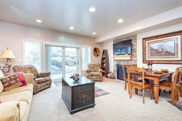 Experience the cozy living room, outfitted with plush seating, a fireplace, an expansive smart TV, and windows that frame the views of the great outdoors.