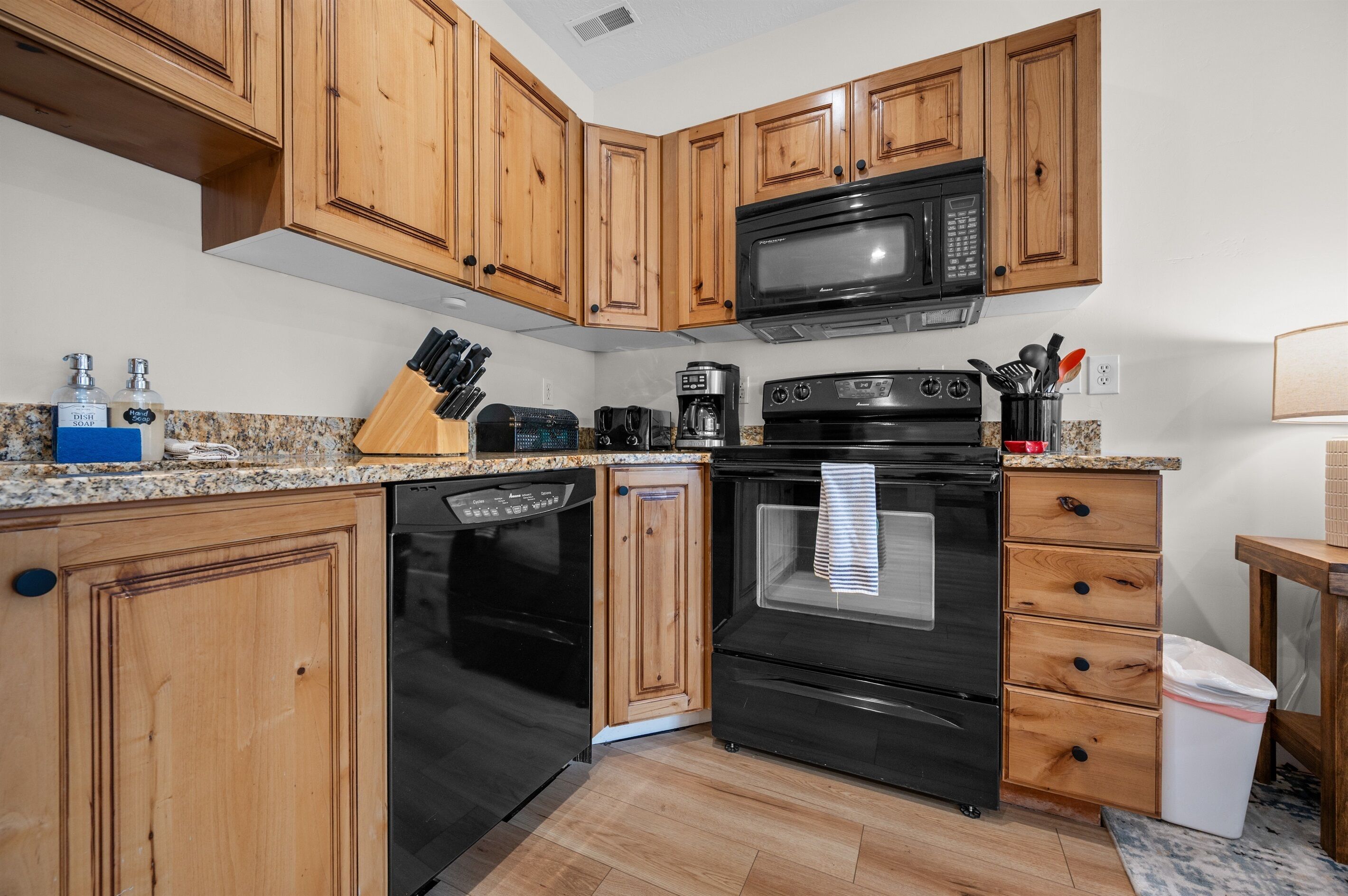 A kitchen with wooden cabinets, a black microwave, a coffee maker, and a dishwasher.