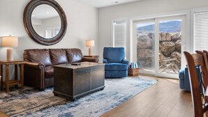 A living room with a brown leather sofa, a blue armchair, a wooden coffee table, and a large mirror on the wall. - Lakeside Escape LS 36B 2 BR |Pineview Res |Hot Tub (Huntsville)