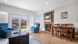 A living room with a fireplace, a TV mounted on the wall, a dining table with chairs, and a blue sofa. - Lakeside Escape LS 36B 2 BR |Pineview Res |Hot Tub (Huntsville)