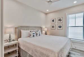 A bedroom with a bed, nightstands, a ceiling fan, and wall art.