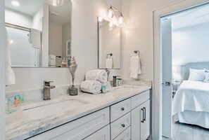 A modern bathroom with a marble sink, a large mirror, and a shower area visible through an open door.