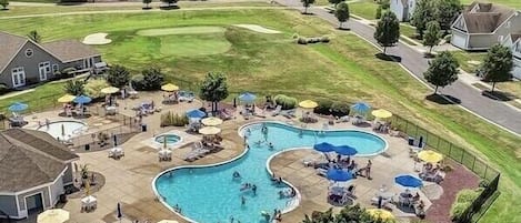 A golf course with a swimming pool area featuring multiple pools, umbrellas, and lounge chairs.