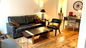 A living room with a leather sofa, a wooden coffee table, a white chair, and a desk with a lamp. - Luxury King Suite, Living Room w/sofa bed and jacuzzi tub (West Dover)