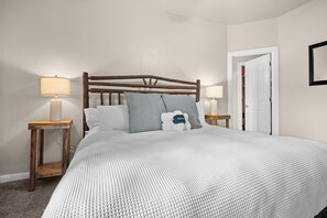 A neatly made bed with a textured white duvet, two bedside tables with lamps, a wooden headboard, and a white door. - Lakeside Escape LS36 |Ski Lodge |Hot Tub | Game Rm (Huntsville)