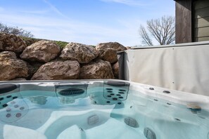 A hot tub with multiple jets, surrounded by large rocks and a building in the background. - Lakeside Escape LS36 |Ski Lodge |Hot Tub | Game Rm (Huntsville)