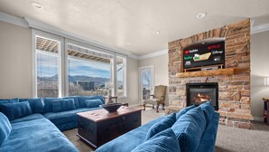 A living room with a stone fireplace, a large sectional sofa, and a flat-screen TV mounted above the fireplace displaying various streaming services.