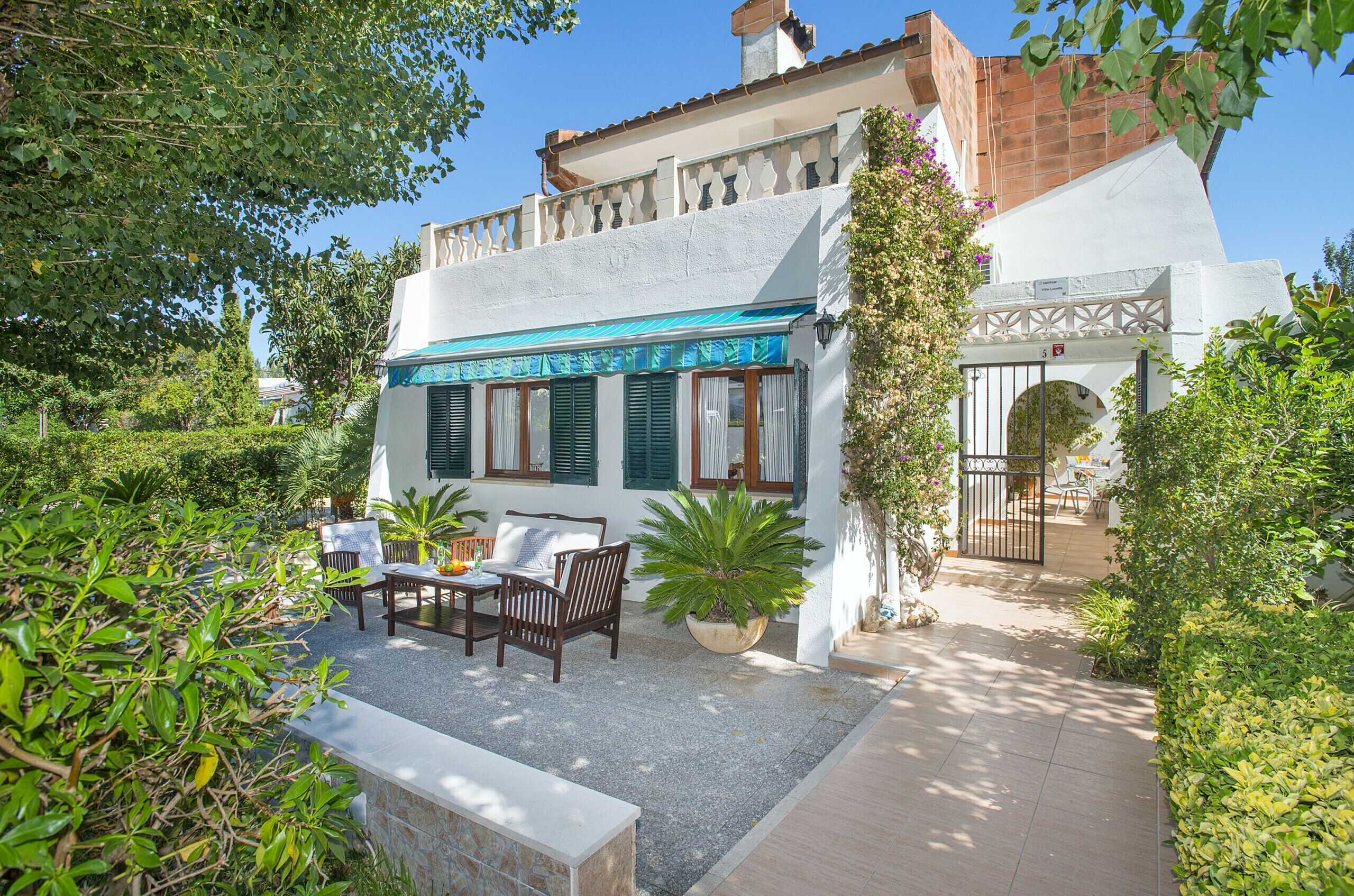 A courtyard with outdoor seating, a potted plant, and a white building with a blue awning.