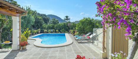 A swimming pool with a pergola, lounge chairs, and potted plants.