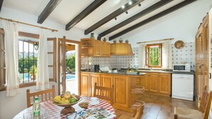 A kitchen with wooden cabinets, a dining table with a red and white checkered tablecloth, and a view of a pool outside. - VILLA MATEU - 5 MIN WALK TO THE OLD TOWN (Pollensa)