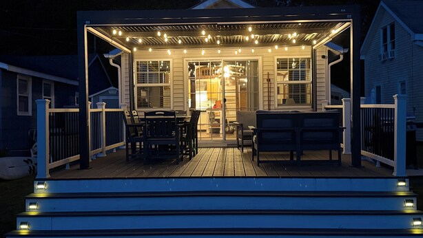 A covered deck with string lights, a table, chairs, and a bench. - Sunset Lover's Dream! Lakefront Cottage on Otisco! (Marietta)