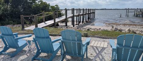 Un espace aménagé avec des sièges au bord de l’eau, comprenant des chaises Adirondack bleues et une jetée en bois qui s’avance dans l’eau.