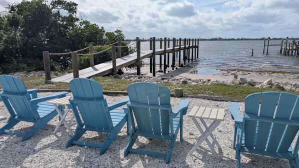 Un área de descanso frente al agua, con sillas Adirondack azules y un muelle de madera que se adentra en el agua.