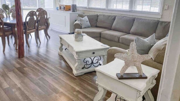 A spacious living room with a wooden floor, a beige sofa, a white coffee table, and a dining area with wooden chairs. - The Comfy Cottage at Possum Kingdom Lake 🚤🐟🌞 (Graford)