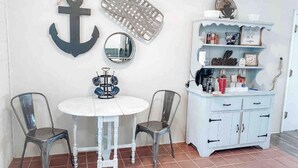 A dining area with a white round table, two metal chairs, a white cabinet with shelves, and decorative items like an anchor and a mirror on the wall. - The Comfy Cottage at Possum Kingdom Lake 🚤🐟🌞 (Graford)