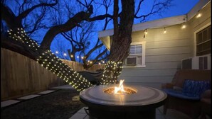 A backyard with a circular fire pit, a wooden fence, and string lights. - The Comfy Cottage at Possum Kingdom Lake 🚤🐟🌞 (Graford)
