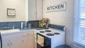 A kitchen with white cabinets, a stove, and a window with blinds. - The Comfy Cottage at Possum Kingdom Lake 🚤🐟🌞 (Graford)