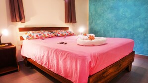 A neatly made bed with a pink bedspread and pillows, a bedside table with a lamp, and a blue wall in the background. - NELLY HOUSE (AP. SANDIA) (SAMARA)