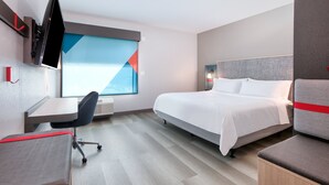 Une chambre d’hôtel moderne équipée d’un lit, d’un bureau, d’une chaise et d’un téléviseur fixé au mur.