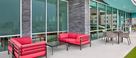 An outdoor seating area with red sofas and a table, large windows, and a green lawn.