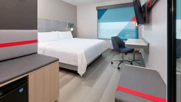 A modern hotel room with a bed, a desk, a chair, and a TV mounted on the wall.