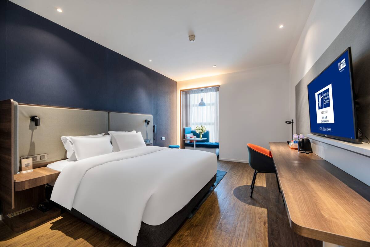 A modern hotel room with a large bed, a desk, and a television.