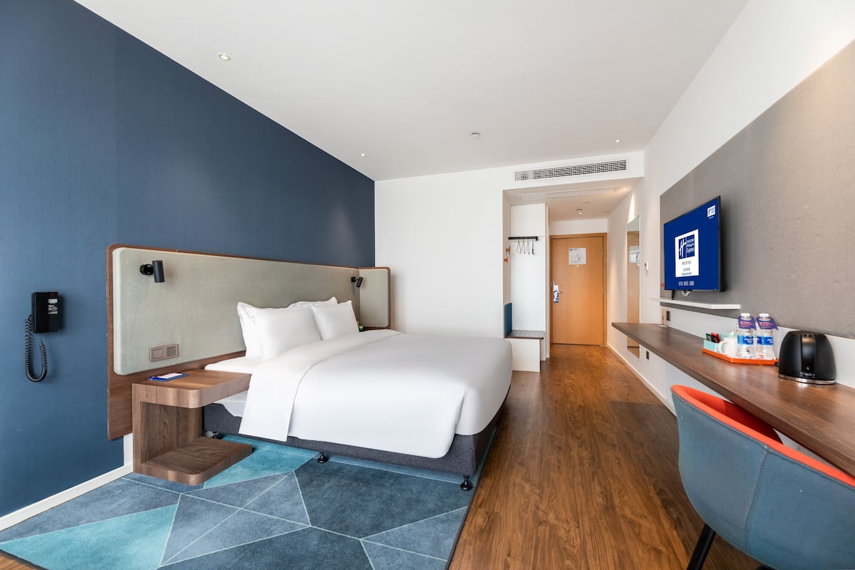 A hotel room with a bed, bedside table, TV, and a desk with a chair.