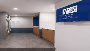 Corredor de hotel estreito com um sofá azul, uma máquina de lavar e uma placa da Holiday Inn Express.