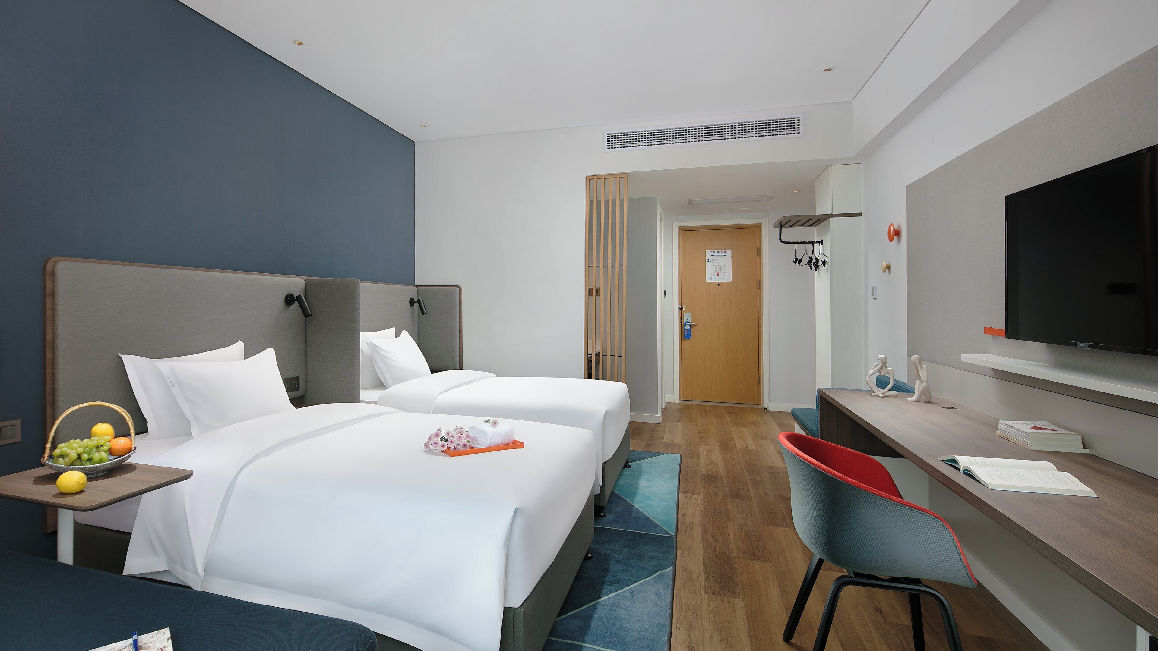 A hotel room with two beds, a desk, a TV, and a bathroom visible through an open door.