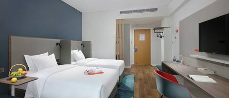A hotel room with two beds, a desk, a TV, and a bathroom visible through an open door.