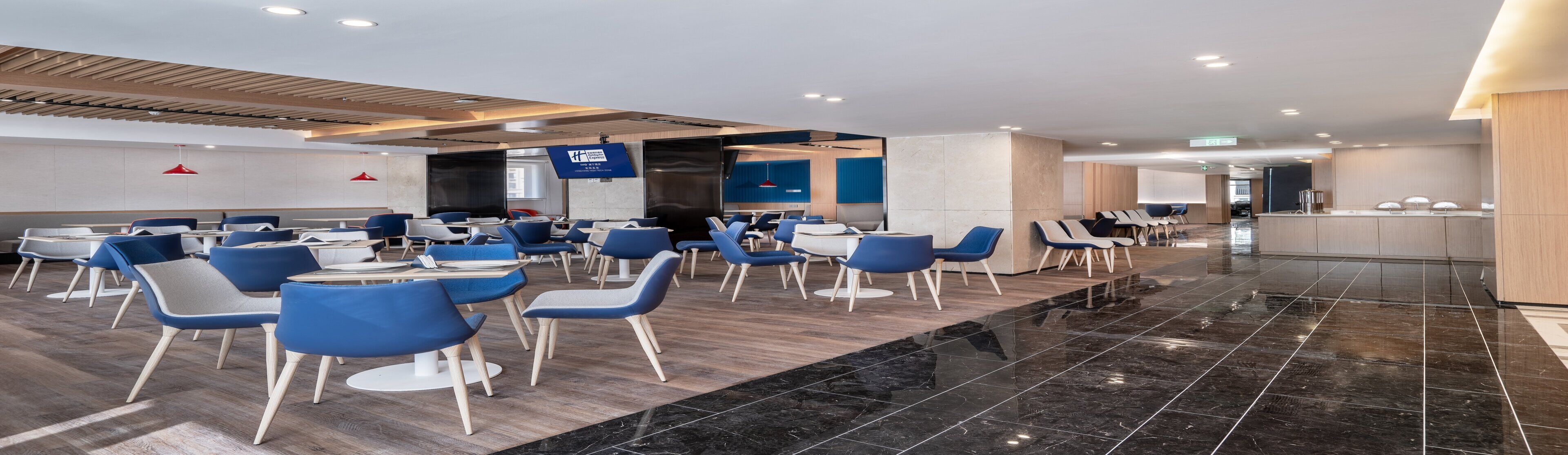 Un hall d’hôtel moderne, aménagé avec différents espaces de détente, notamment des tables et des chaises, ainsi qu’un comptoir d’accueil.
