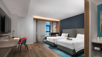 Une chambre d’hôtel moderne équipée d’un bureau, de deux lits, d’une télévision et offrant une vue sur la ville.