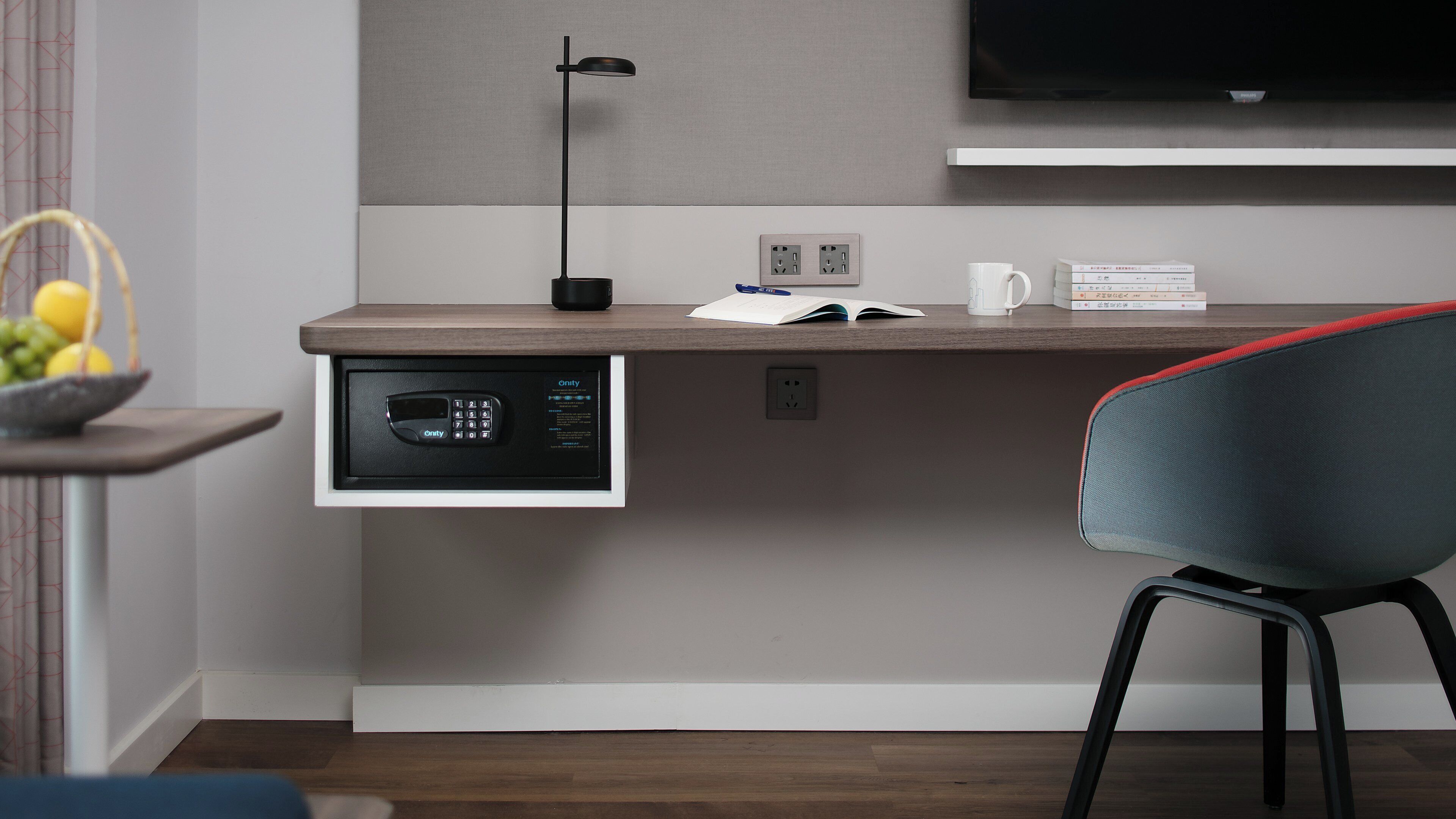 Une chambre d’hôtel moderne équipée d’un bureau, d’une chaise, d’un téléviseur à écran plat et d’un coffre-fort intégré.