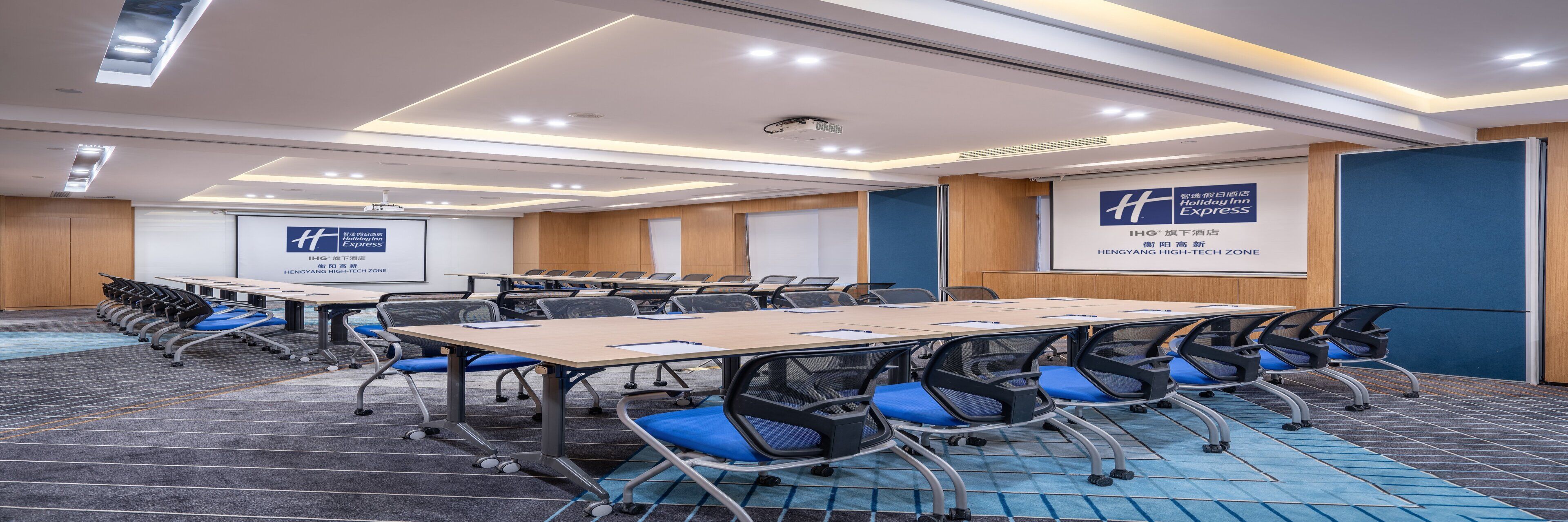 A conference room with multiple tables and chairs, a projector screen, and a sign indicating the location as HENGYANG HIGH-TECH ZONE.