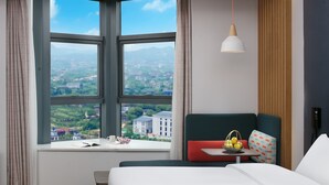 A hotel room with a large window offering a city view, a bed, a bedside table with a basket of fruit, and a hanging pendant light. - Holiday Inn Express Hengyang High-Tech Zone by IHG (Hengyang)