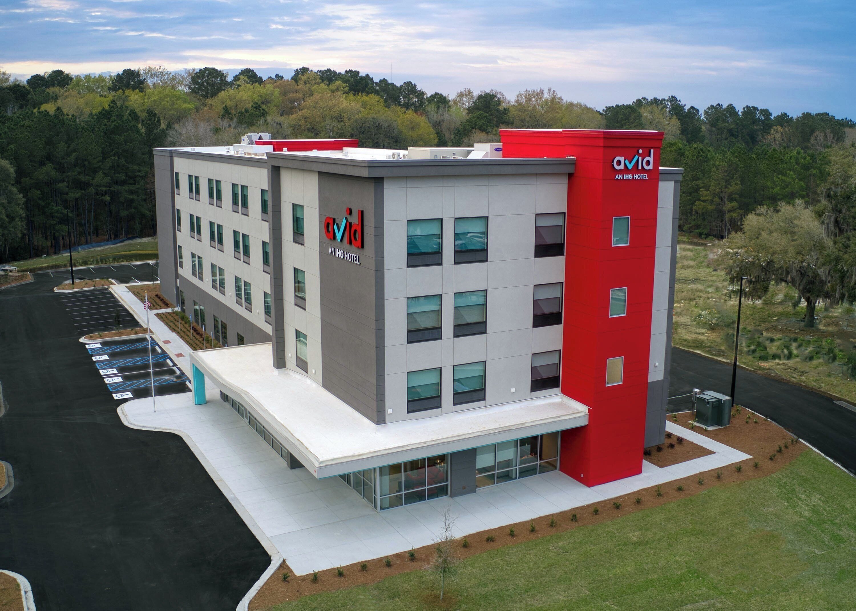 Um hotel moderno com fachada em vermelho e cinza, vários andares e estacionamento.