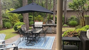 An outdoor patio with a brick floor, a table with chairs, a grill, and a large umbrella. - The Mulligan House in the heart of Pinehurst, NC. (Pinehurst)