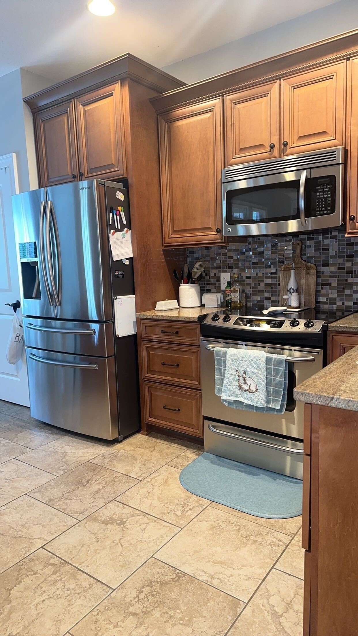 A kitchen with stainless steel appliances, wooden cabinets, a tiled backsplash, and a granite countertop.