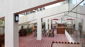 Un espacio al aire libre con piso de madera, plantas en macetas y mobiliario exterior.