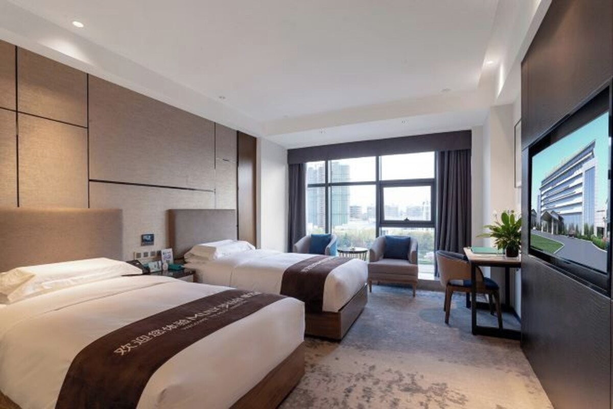Habitación de hotel con dos camas, un escritorio, una silla, un televisor y un ventanal grande.