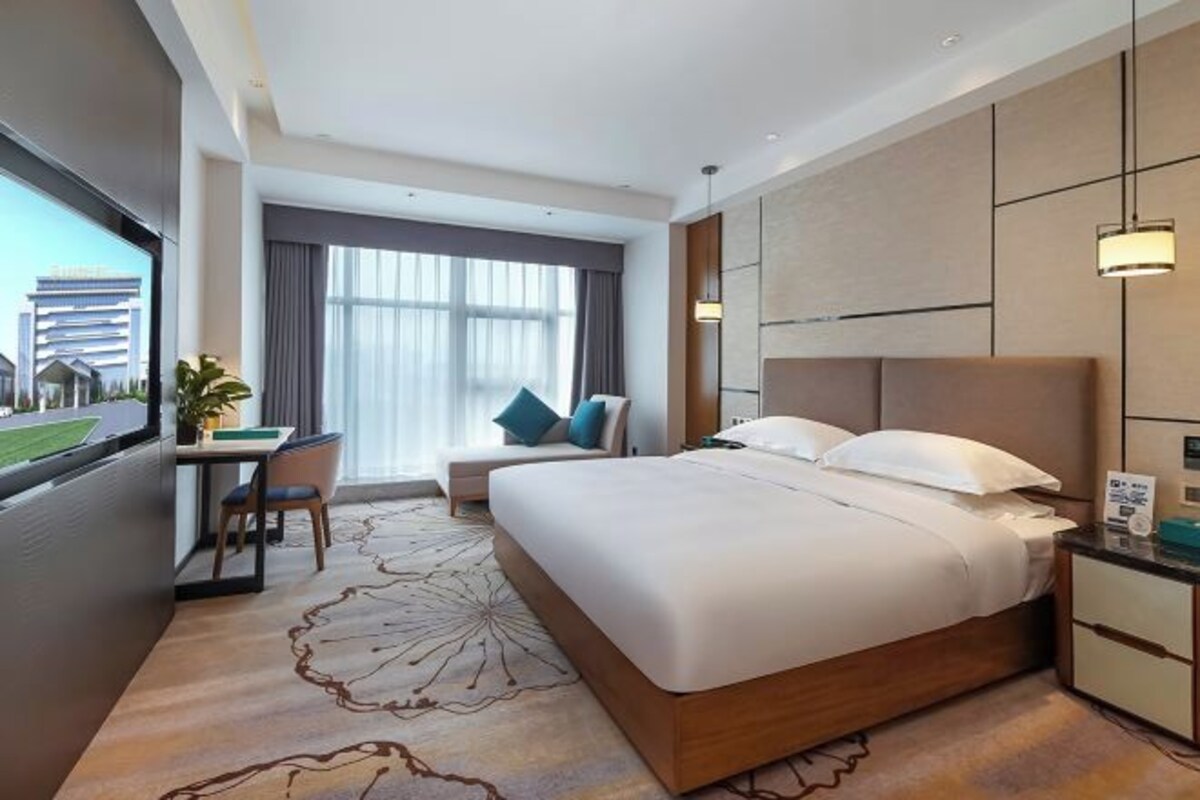 Habitación de hotel moderna con una cama grande, un escritorio y vistas a un paisaje urbano.