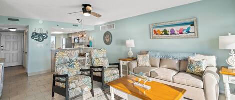 A living room with a beige sofa, floral armchairs, a wooden coffee table, and a ceiling fan.