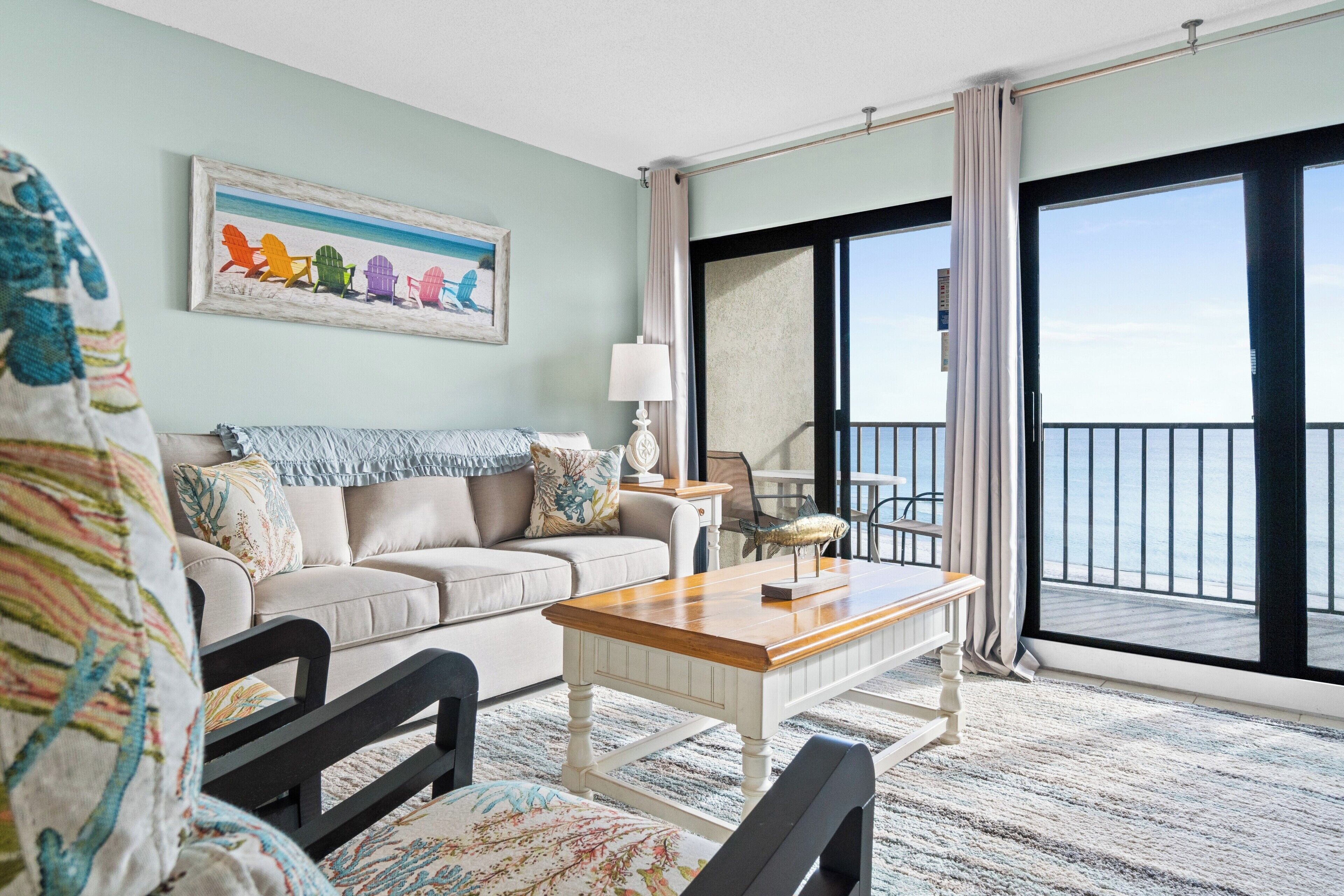 A room with a sofa, a wooden coffee table, and a view of the sea through a large sliding glass door.