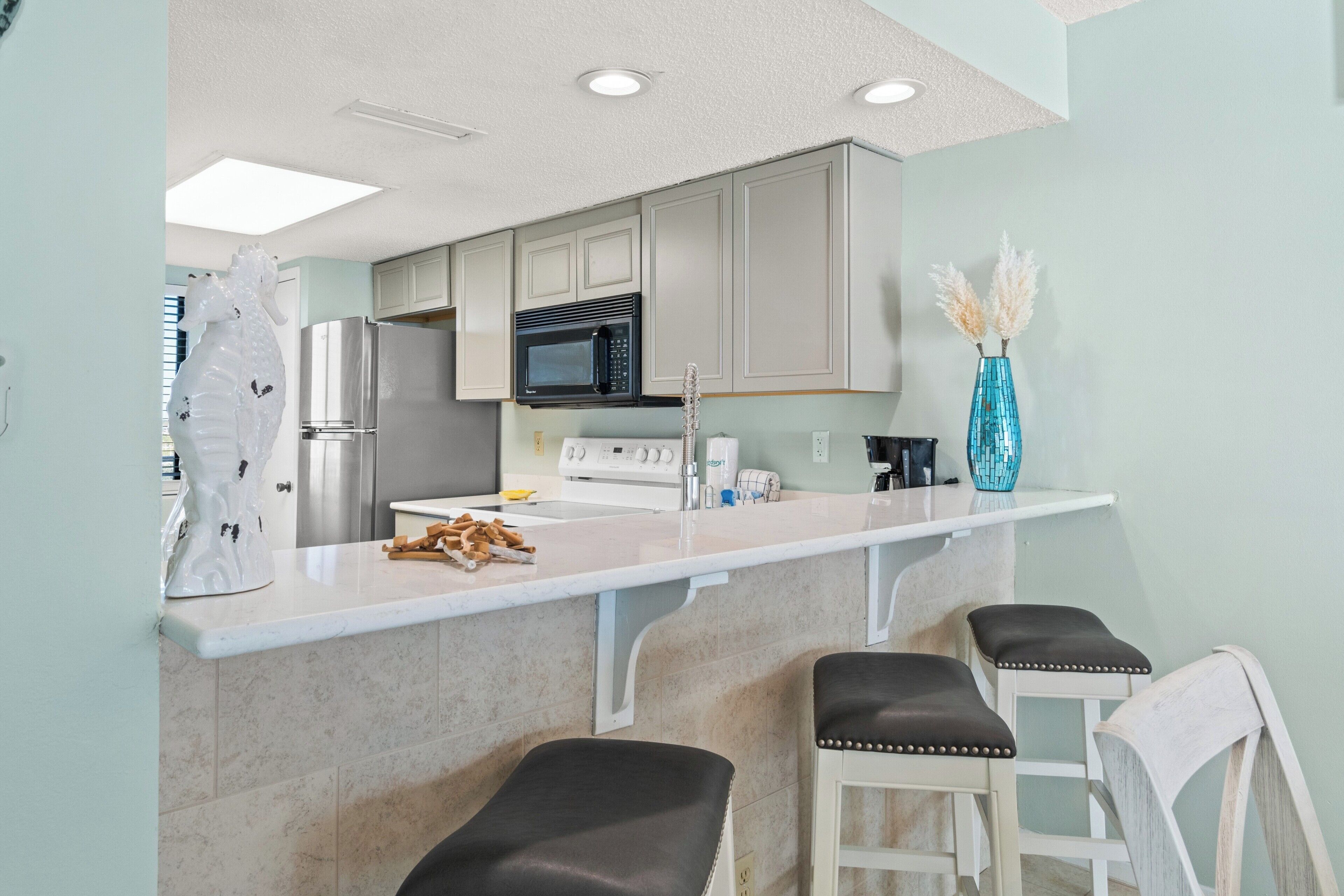 A kitchen with a white countertop, stainless steel appliances, and a blue vase with pampas grass.