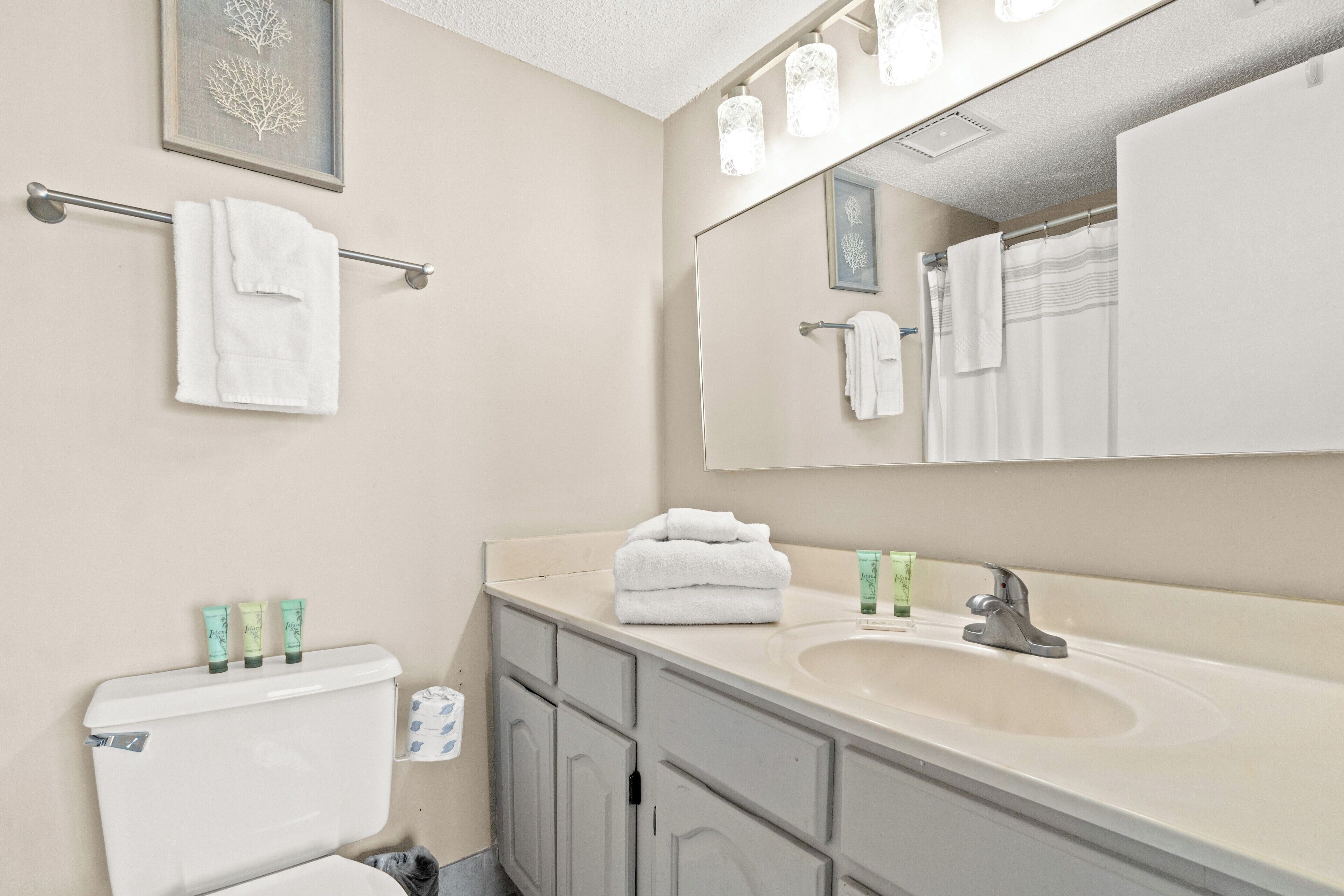 A bathroom with a toilet, sink, and mirror. There are towels on the towel rack and a glass of water on the sink.