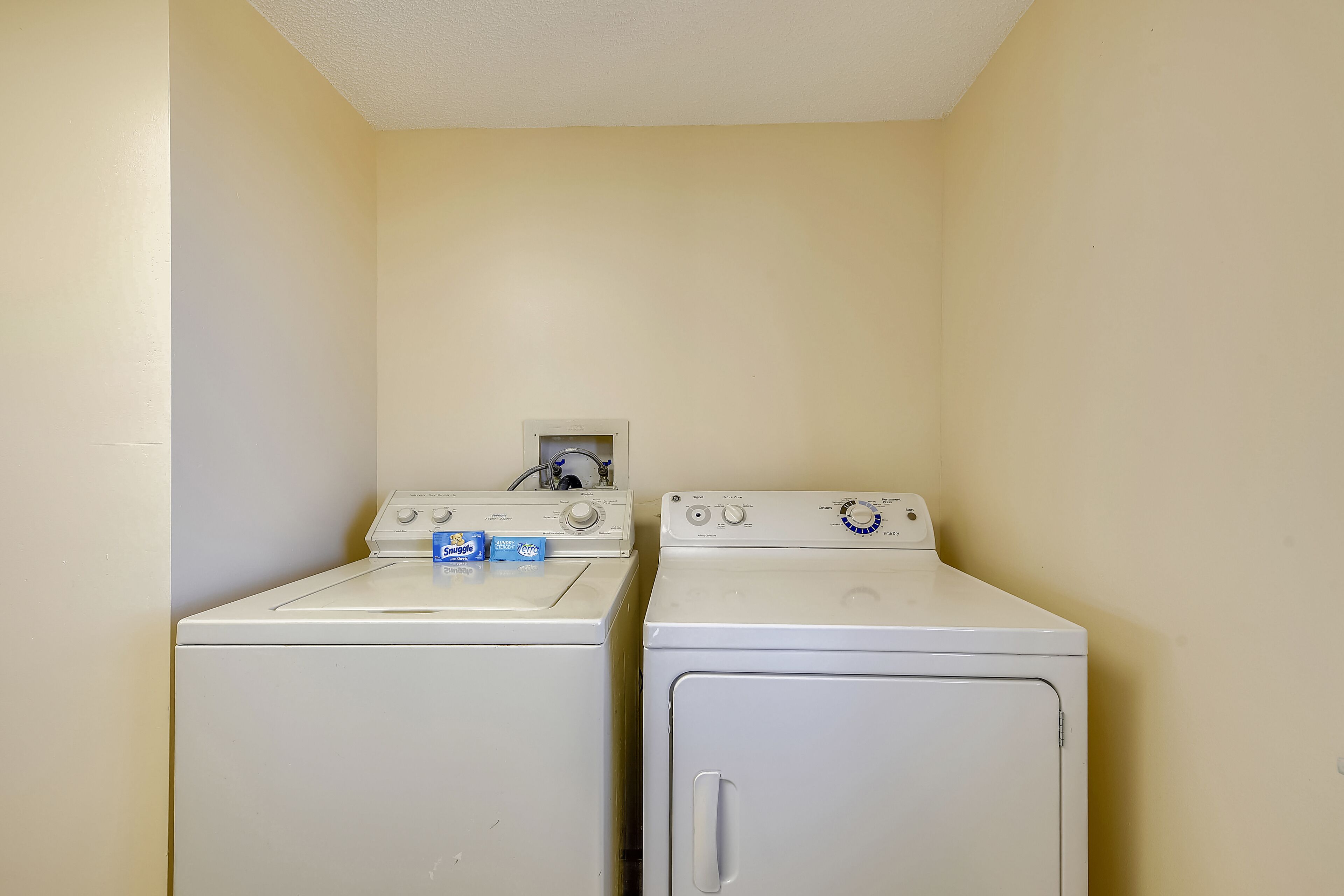 A laundry room with two stacked washers and dryers, a control panel, and two detergent boxes.